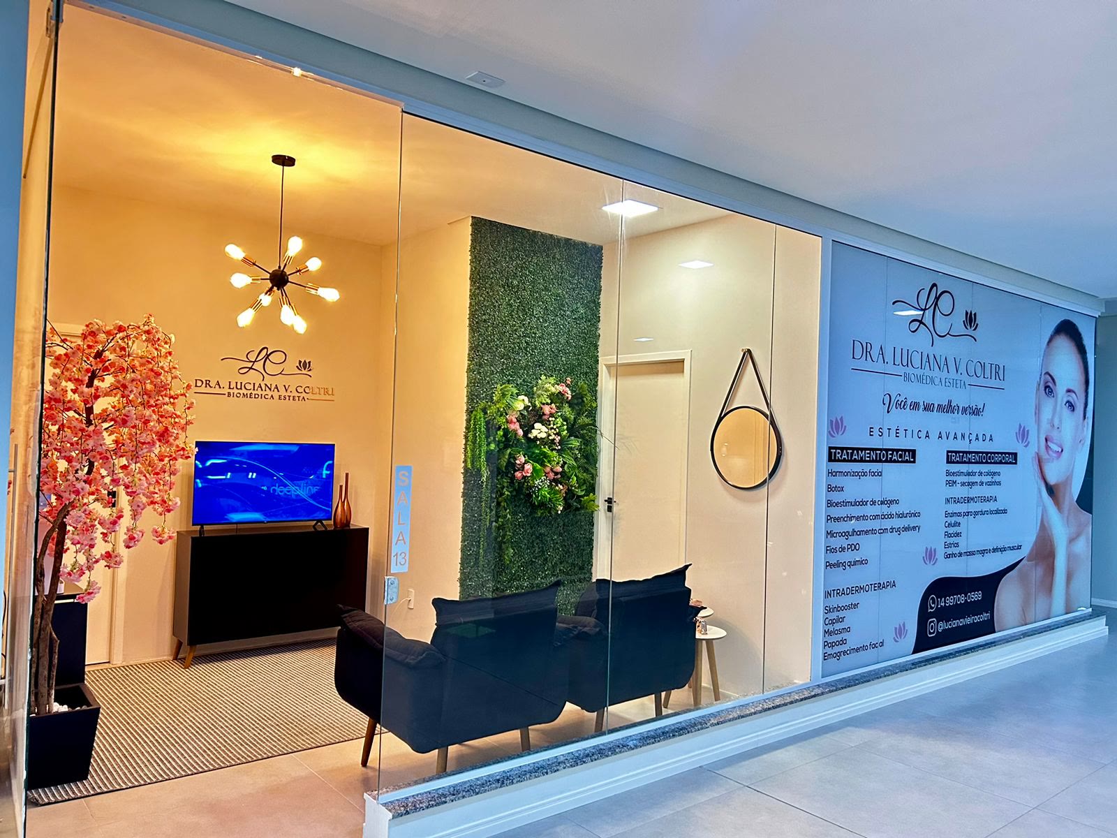 A sala da clínica vista de fora, pela vitrine de vidro, com a cerejeira, a parede verde e o painel da Dra. Luciana